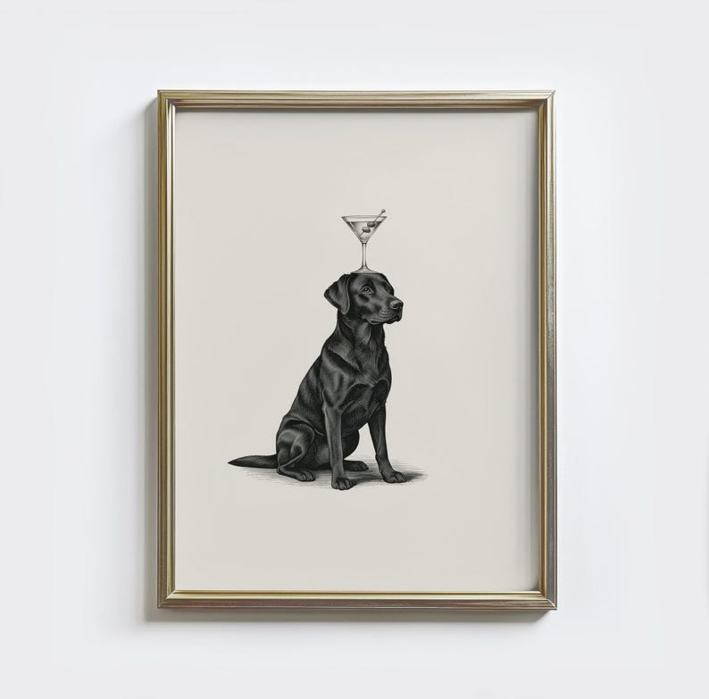 May include: A framed print featuring a black Labrador Retriever with a martini glass balanced on its head. The dog is sitting, and the martini glass has a green olive. The frame is gold.