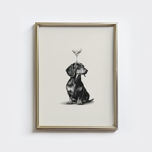 May include: Framed black and white print of a dachshund dog with a martini glass balanced on its head. The dog is sitting, and the martini glass has an olive. The print is in a gold frame.
