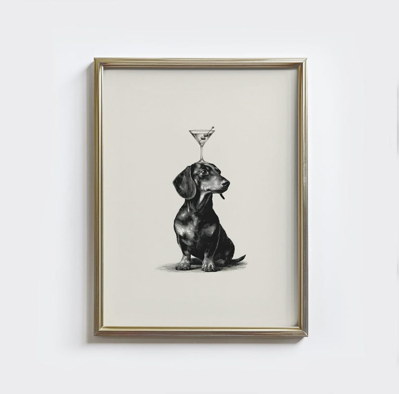 May include: Framed black and white print of a dachshund dog with a martini glass balanced on its head. The dog is sitting, and the martini glass has an olive. The print is in a gold frame.