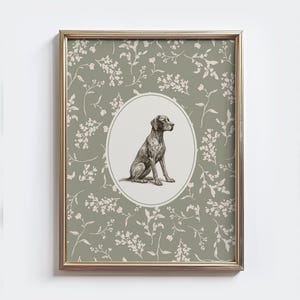 Può includere: Stampa incorniciata con un'illustrazione dettagliata di un cane all'interno di una cornice ovale. Il cane è raffigurato in posizione seduta, con una tavolozza di colori neutri. Lo sfondo è un motivo floreale nei toni del verde e del bianco, il tutto racchiuso in una cornice dorata.