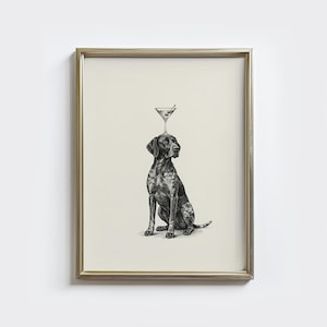 May include: Framed black and white print of a dog balancing a martini glass on its head. The dog is a German Shorthaired Pointer, with a speckled coat. The martini glass has an olive. The print is in a gold frame.