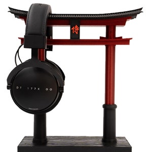 May include: Black headphones with a black stand and a red Japanese torii gate. The headphones have the text "DT 177X GO" on the side. The torii gate has the Japanese character "待" on it.