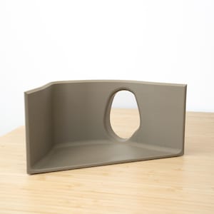 Pu&ograve; includere: Un oggetto di forma geometrica a tre lati, di colore marrone chiaro, con un'apertura curva. L'oggetto &egrave; realizzato in un materiale liscio e opaco e si trova su una superficie di legno chiaro.