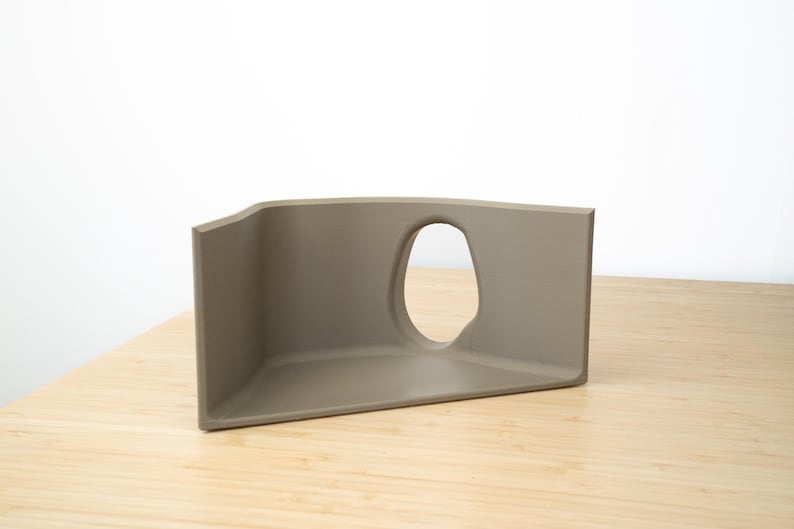 Pu&ograve; includere: Un oggetto di forma geometrica a tre lati, di colore marrone chiaro, con un'apertura curva. L'oggetto &egrave; realizzato in un materiale liscio e opaco e si trova su una superficie di legno chiaro.