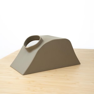 Pu&ograve; includere: Un oggetto in ceramica marrone chiaro con una forma curva e un foro nella parte superiore. L'oggetto &egrave; posto su una superficie di legno.