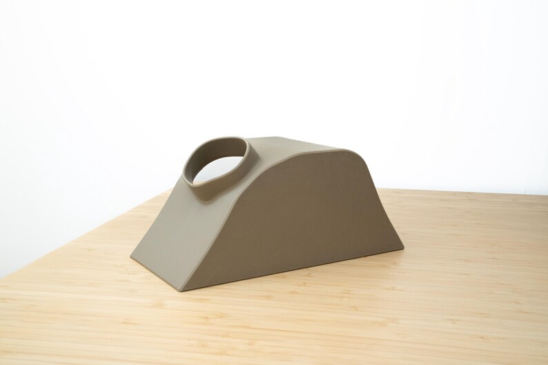 Pu&ograve; includere: Un oggetto in ceramica marrone chiaro con una forma curva e un foro nella parte superiore. L'oggetto &egrave; posto su una superficie di legno.
