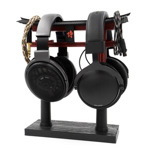 May include: Two black headphones with black stands on a wooden base. The headphones are resting on a red and black stand with the Japanese character "信" written on it.