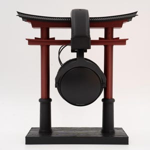 May include: Black headphones with a black headband hanging from a red and black wooden stand shaped like a Japanese torii gate.