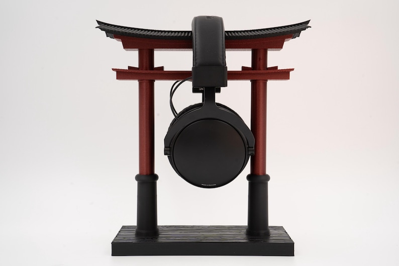May include: Black headphones with a black headband hanging from a red and black wooden stand shaped like a Japanese torii gate.