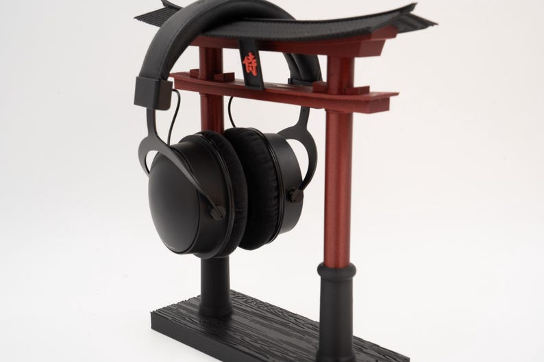 May include: Black headphones with a black and red torii gate stand. The stand has a wooden base and the torii gate has the kanji character for "lucky" written on it.