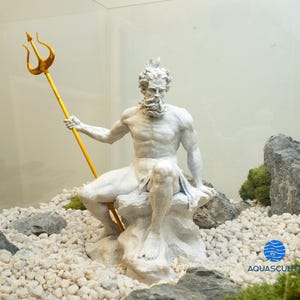 以下が含まれることがあります： 白い樹脂製のポセイドン像。ギリシャの海の神ポセイドンが、金の三叉槍を持って岩に座っている。像は白い小石と緑の苔に囲まれている。