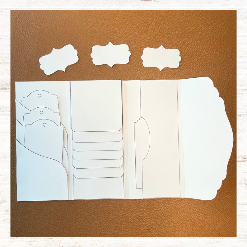 K&ouml;nnte beinhalten: Ein wei&szlig;es Papierbastelprojekt mit mehreren Taschen, Laschen und Etiketten. Das Projekt ist zum Organisieren und Aufbewahren von kleinen Gegenst&auml;nden gedacht.