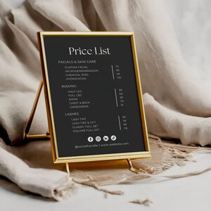 Puede incluir: Un cartel negro enmarcado con un marco dorado, que enumera los precios de varios servicios de belleza, incluyendo tratamientos faciales, depilaci&oacute;n con cera y pesta&ntilde;as. El cartel est&aacute; en un soporte dorado y tiene un fondo blanco.