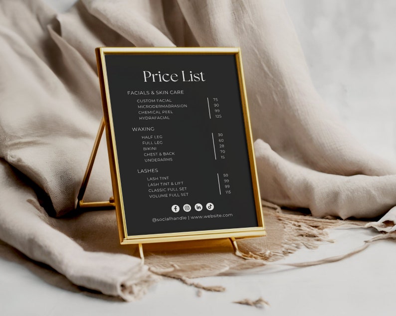 Puede incluir: Un cartel negro enmarcado con un marco dorado, que enumera los precios de varios servicios de belleza, incluyendo tratamientos faciales, depilaci&oacute;n con cera y pesta&ntilde;as. El cartel est&aacute; en un soporte dorado y tiene un fondo blanco.