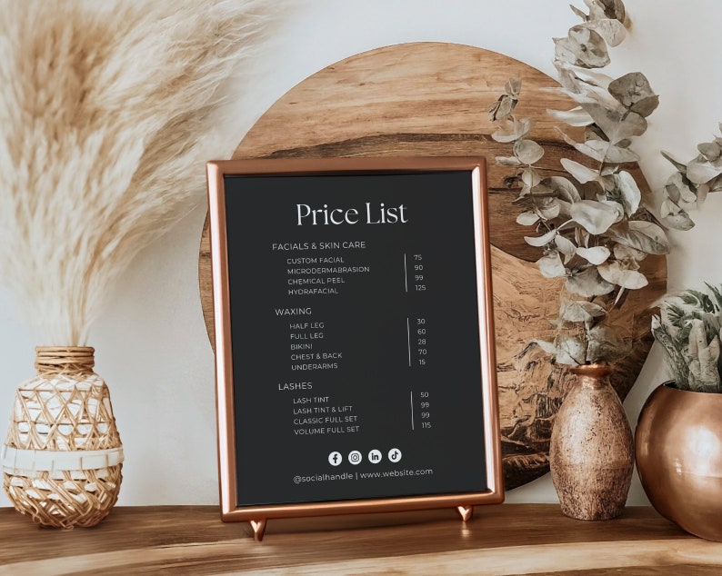 Puede incluir: Un letrero de pizarra negra con marco y soporte de cobre, que muestra una lista de precios para tratamientos faciales, depilaci&oacute;n con cera y servicios de pesta&ntilde;as. El letrero est&aacute; sobre una superficie de madera con hierba de la pampa seca y ramas de eucalipto en jarrones.