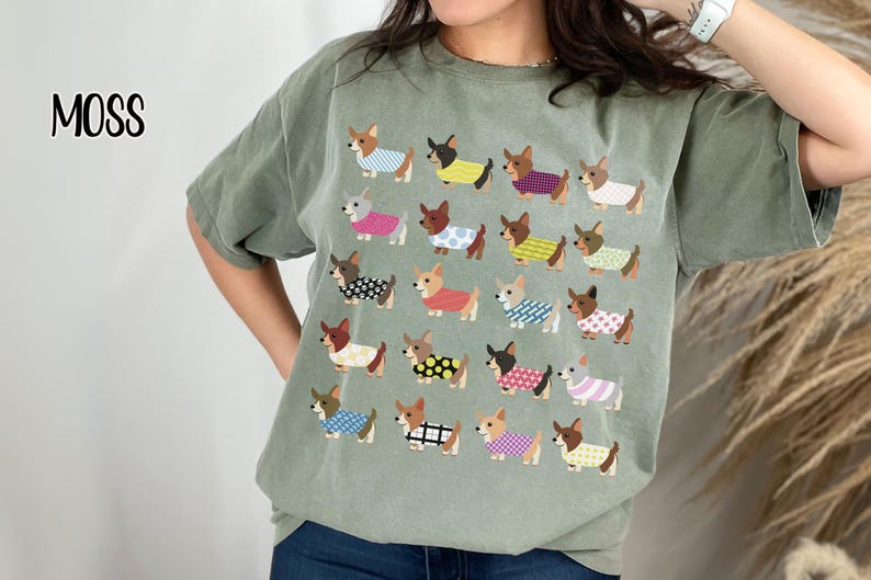 May include: Moss green t-shirt featuring a repeating pattern of cartoon dachshunds wearing various outfits. The word "MOSS" is printed in black script in the upper left corner. The shirt is a relaxed fit.