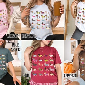 May include: A collection of t-shirts in various colors, each featuring a repeating pattern of dachshund dogs in different outfits. Colors include pink, blue, white, green, red, and brown. The text on the shirts reads "Blossom", "Chambray", "Gildan White", "Blue Spruce", "Chili", and "Espresso".