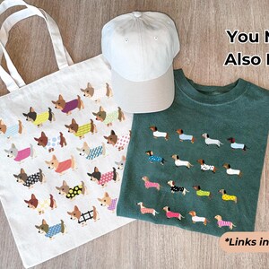 May include: A white tote bag, a light gray baseball cap, and a green t-shirt are displayed. The tote bag and t-shirt feature a repeating pattern of dachshunds wearing various outfits. The text "You May Also Like" and "*Links in description" are also visible.