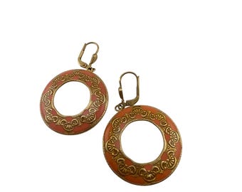 May include: A pair of hoop earrings with a coral-colored enamel center and a decorative gold-tone metal border. The earrings have a lever-back closure and a circular design. The earrings are a vintage style.