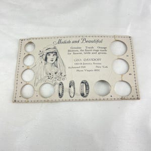 May include: Vintage ring display card with the text "Modish and Beautiful." The card features an illustration of a woman in a veil and three ring designs. The card has several circular cutouts for ring display.