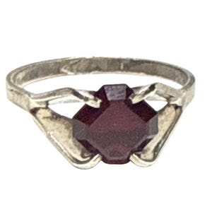 Puede incluir: Un anillo de plata con una piedra preciosa de color rojo oscuro, tallada en forma cuadrada. La banda del anillo tiene un diseño sencillo, con elementos decorativos a ambos lados de la piedra preciosa, creando un aspecto clásico y elegante.