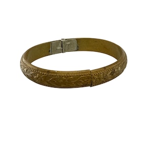 Puede incluir: Una pulsera brazalete dorada vintage con un patrón floral grabado. La pulsera con bisagras presenta un cierre seguro. El diseño incluye motivos detallados de hojas y vides, creando una estética antigua. La pulsera es una pieza de joyería clásica.