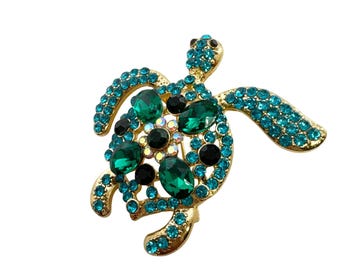 May include: A gold-toned metal turtle brooch with turquoise and green gemstones. The turtle's shell features large green and black stones, while the body and flippers are adorned with smaller turquoise gems. A unique jewelry accessory.