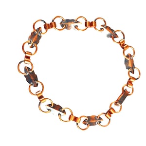 May include: A copper chain necklace with leaf-shaped links. The chain is made of small, round links that are connected to larger, leaf-shaped links. The necklace is a simple and elegant design.