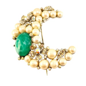May include: A silver crescent moon brooch with faux pearls, a green cabochon stone, and sparkling rhinestones.