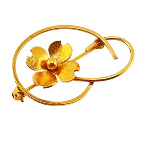 以下が含まれることがあります： 円形のフレームにスタイリッシュな花のデザインが施されたゴールドトーンのブローチ。花は5枚の花びらと小さな丸い中心を持っています。