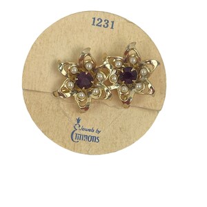 May include: Vintage gold-tone flower earrings with a central purple stone and small white pearls. The earrings are on a tan card with the number 1231 and the "Jewels by Emmons" logo.