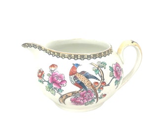 Könnte beinhalten: Ein weißer Keramik-Milchkännchen mit goldfarbenem Rand und einem Blumendesign mit einem Fasan und rosa Blüten.