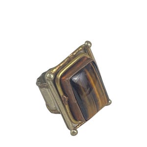 May include: A gold and silver ring with a rectangular tiger's eye stone.