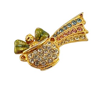 May include: A gold-tone brooch with a green shamrock and a rainbow design. The shamrock is set with clear rhinestones and the rainbow is made of colorful enamel.