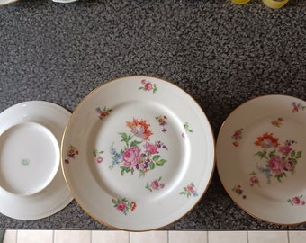 May include: Three white porcelain plates with gold trim and floral designs. The largest plate has a larger floral design in the center and smaller floral designs around the edge. The two smaller plates have smaller floral designs in the center.