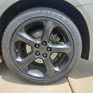 May include: A black car tire with a black rim and Goodyear Eagle Touring tires. The tire has a black valve stem cap.