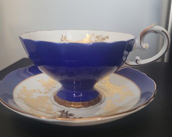 May include: A blue and white teacup and saucer set with gold accents. The teacup has a scalloped rim and a delicate floral design. The saucer has a matching design.