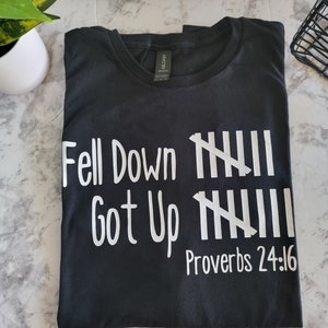 Puede incluir: Camiseta negra con texto blanco que dice "Fell Down  ||||| Got Up ||||| Proverbs 24:16"