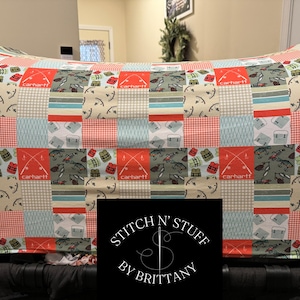 May include: A red, white, and blue patchwork fabric with a fishing theme. The fabric features a repeated pattern of fishing rods, fish, and Carhartt logos. The fabric is displayed on a black stroller.