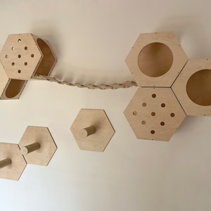 May include: A wall-mounted cat tree made of natural wood with hexagonal shelves, a rope bridge, and scratching posts. The cat tree is designed to provide cats with a variety of activities, including climbing, scratching, and lounging.