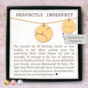 Può includere: Collana d'oro con un ciondolo rotondo che presenta un designo di crepa. Il ciondolo è su uno sfondo bianco con il testo "Perfectly Imperfect" e una citazione sul Kintsugi, l'arte giapponese di riparare la ceramica rotta con l'oro. L'incisione opzionale sul retro dice "Ti amo".