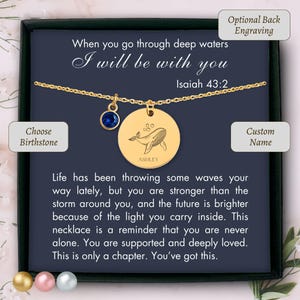 May include: A gold-colored necklace with a round pendant featuring a whale illustration and the name "ASHLEY". It includes a blue birthstone charm and is presented in a gift box with inspirational text. The text reads "When you go through deep waters I will be with you".
