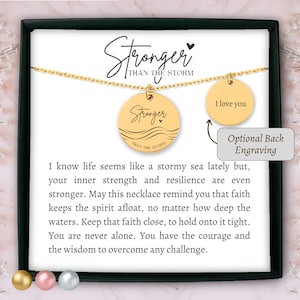 Può includere: Collana dorata con due ciondoli circolari. Uno recita "Stronger Than The Storm", l'altro "I love you". La collana è esposta su una carta bianca con testo motivazionale.