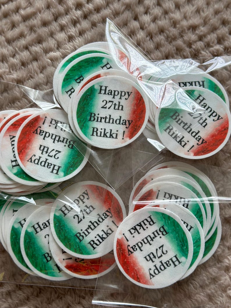 May include: A collection of round stickers with a green, white, and red color scheme, resembling a flag. Each sticker has the text "Happy 27th Birthday Rikki!" printed on it. The stickers are packaged in clear plastic.