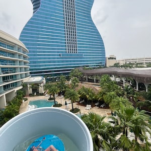 May include: A blue and white cup filled with ice and a decorative disc that says "Happy Birthday" with a woman on it. In the background is a guitar-shaped building and palm trees.