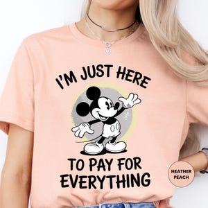 a woman wearing a pink shirt with a mickey mouse saying i'm just here