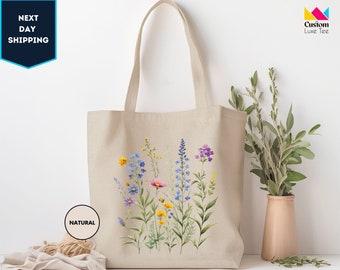 May include: A natural canvas tote bag with a floral design featuring blue, pink, yellow, and green flowers. The bag has long straps and is perfect for carrying groceries or other items.