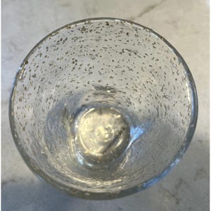 May include: A clear, round glass with a speckled, textured surface. The glass has a wide opening and a slightly curved base. The interior of the glass is visible, and the speckled pattern appears throughout the glass.