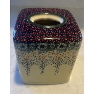 Pode incluir: Caixa de lenços de cerâmica quadrada com uma parte superior azul marinho e vermelha pontilhada. As laterais apresentam padrões florais e de pontos em creme, azul e laranja. A abertura é contornada em verde. Um item decorativo e funcional para a casa.