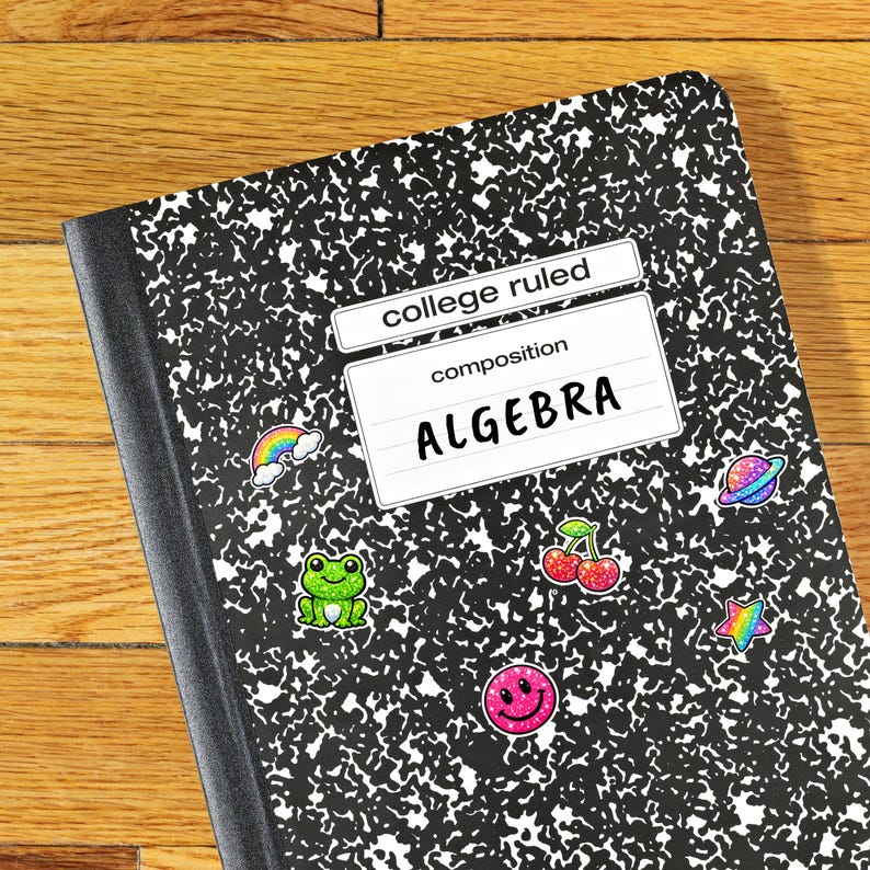 K&ouml;nnte beinhalten: Ein Notizbuch mit einer schwarz-wei&szlig; gesprenkelten H&uuml;lle. Das Etikett lautet "college ruled" und "ALGEBRA". Bunte Aufkleber eines Regenbogens, eines Frosches, Kirschen, eines Smiley-Gesichts, eines Planeten und eines Sterns schm&uuml;cken das Cover.